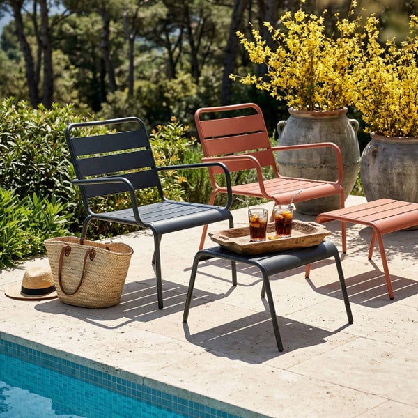 Moderne Gartenstühle und Hocker aus Metall auf einer Terrasse am Pool, mit Getränken auf einem Tablett, einer Strohtasche und gelben Blumen.