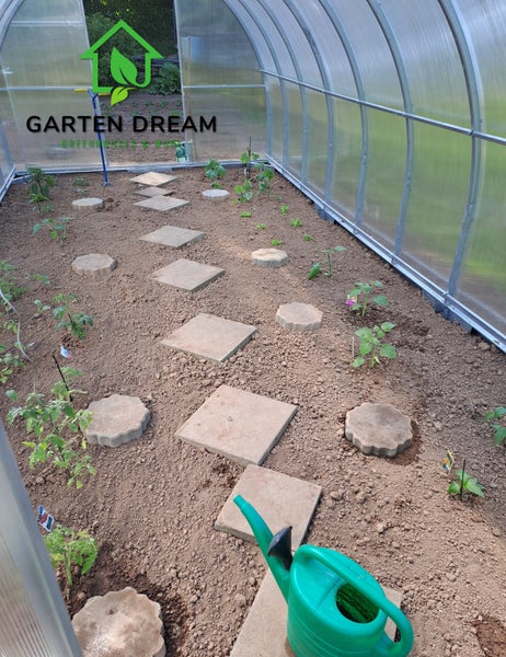 Gewächshaus mit Gemüsebeet, Steinplattenweg und Gießkanne