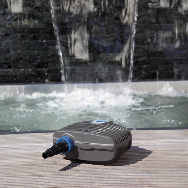 Teichpumpe auf einem Holzdeck vor einem modernen Wasserfall mit einer Wand aus dunklem Naturstein.