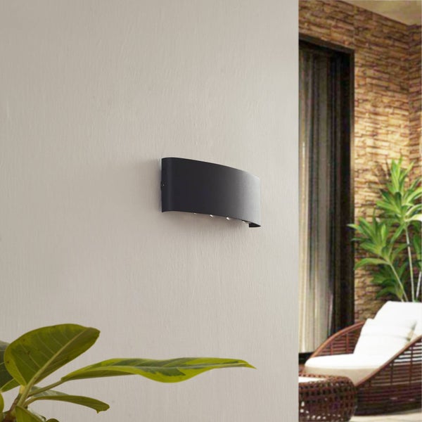 Moderne schwarze gewölbte Wandleuchte auf strukturierter Wand im Außenbereich, neben Terrasse mit Gartenmöbeln und Pflanzen.