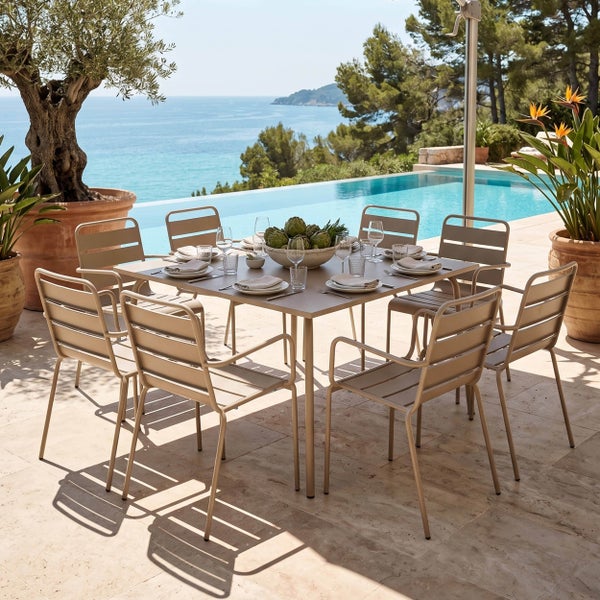 Moderner Gartentisch aus Metall mit acht Armlehnenstühlen auf einer hellen Terrasse neben einem Pool mit Meerblick.