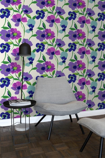 Ein Wohnraum mit einer floral gemusterten Tapete in Blau-, Lila- und Grüntönen, einem grauen Sessel, einem Beistelltisch und einer Stehlampe.