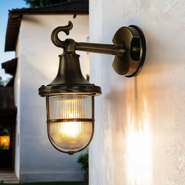 Bronzefarbene Wandleuchte mit klarem Glas und dekorativem Haken an einer weißen Wand