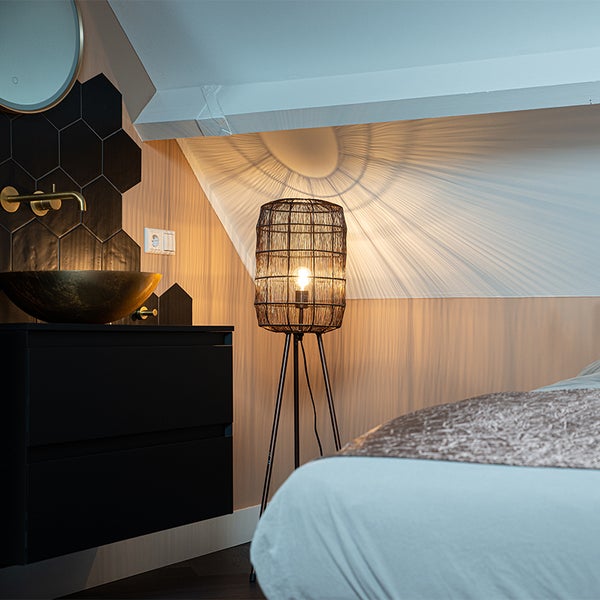 Schlafzimmer mit Waschtisch und einer Stehlampe mit Lampenschirm aus Metalldraht