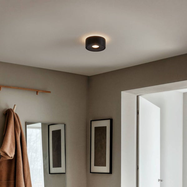 Moderner schwarzer Deckenstrahler in Zylinderform in einem schlichten Flur mit neutralen Wänden und einem Spiegel.