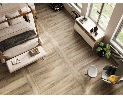 Blick auf ein Schlafzimmer mit Holzboden, Bett, Sessel und Kommode.