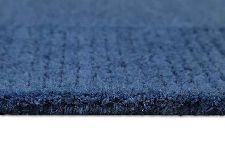 Blauer Teppich mit texturiertem geometrischem Muster und einem kleinen schwarzen Beistelltisch mit Metallbeinen.