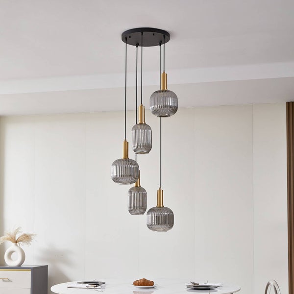 Fünfflammige Pendelleuchte mit geriffelten Glasschirmen in verschiedenen Höhen über einem weißen Esstisch.