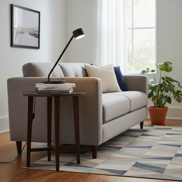 Moderne Schreibtischleuchte auf einem kleinen Holztisch neben einem Sofa in einem hellen Wohnzimmer mit Zimmerpflanze.