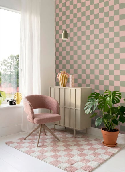 Modernes Zimmer mit einer Vliestapete im Schachbrettmuster in Rosa und Grün, einem rosa Polstersessel und einem passenden karierten Teppich.