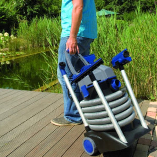 Person zieht einen fahrbaren Teichschlammsauger auf einem Holzsteg neben einem Gartenteich.