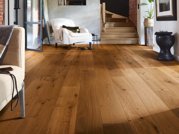 Wohnzimmer mit rustikalem Eichenparkett in Dielenoptik. Helles, modernes Interieur mit Treppe, Sessel und Dekoration auf einem Holzfußboden.