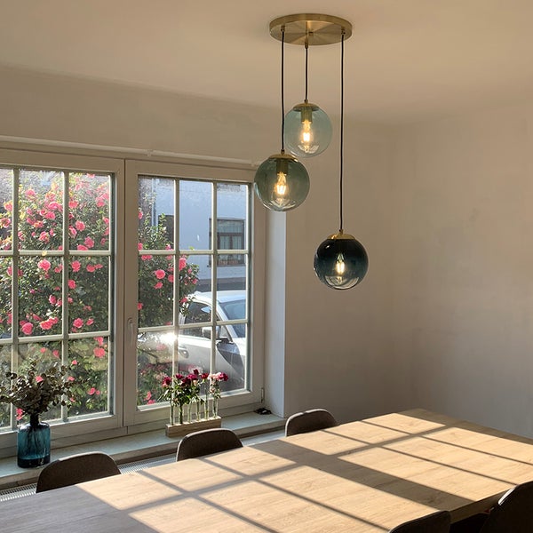 Hängelampe mit drei runden Glasschirmen über einem Esstisch