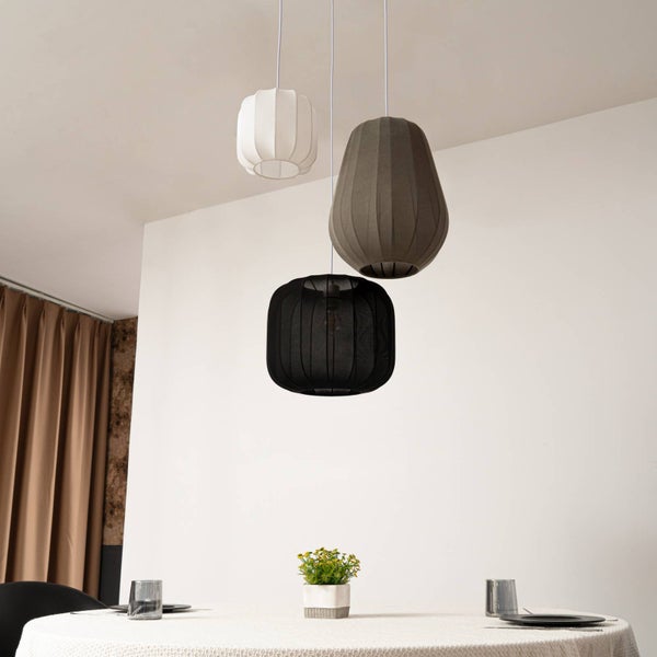 Drei Stoffpendelleuchten in verschiedenen Formen und Höhen hängen über einem runden Esstisch in einem hellen Raum.