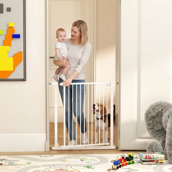 Weißes Schutzgitter für Kinder und Haustiere in einem Türrahmen. Eine Frau mit Baby und ein Hund in einem hellen Kinderzimmer.