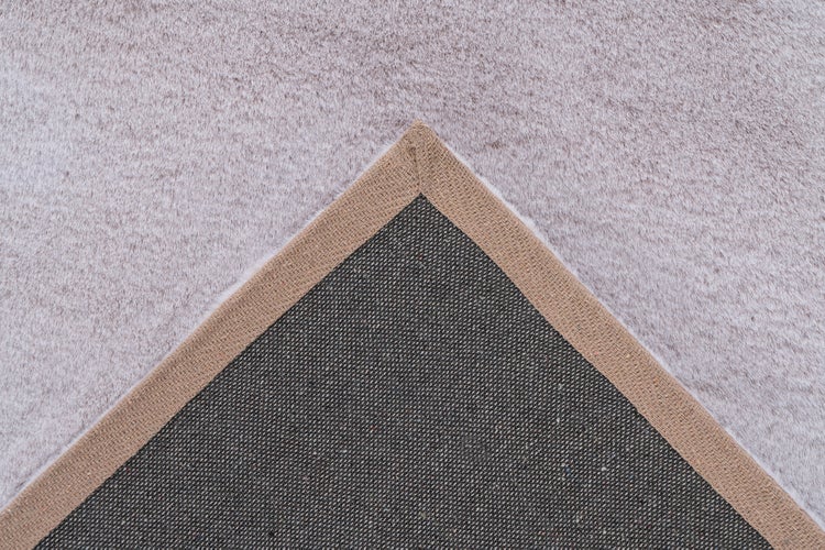 Detailansicht der gewebten Rückseite und der weichen Oberseite eines Teppichs mit eingefasster Kante.