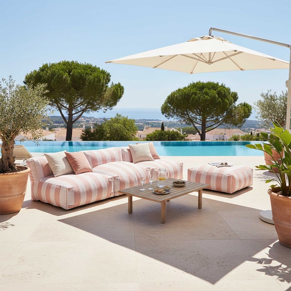Heller Outdoor-Loungebereich mit gestreiftem Sofa, Hocker, Holztisch und Sonnenschirm an einem Pool mit Olivenbäumen.