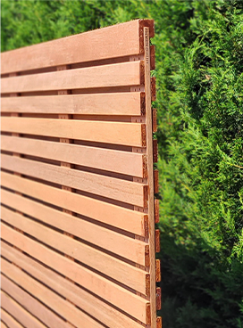 Sichtschutzzaun aus Holz mit horizontalen Lamellen vor einer grünen Hecke.
