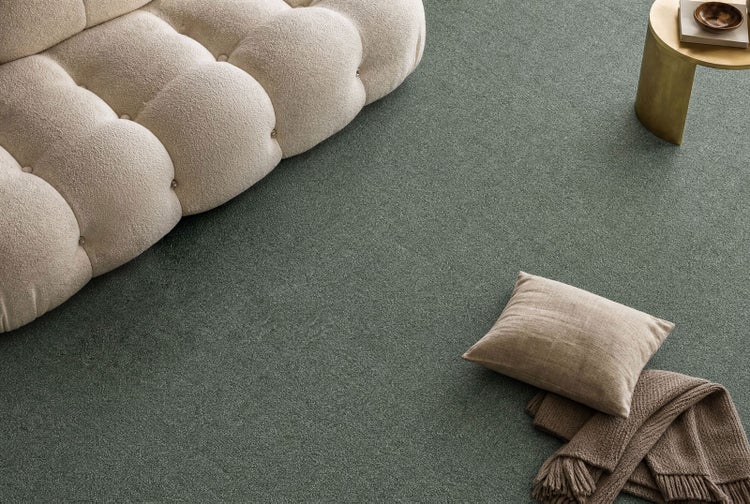 Strukturierter Teppichboden in einem Wohnzimmer mit einem gesteppten Sofa, einem kleinen Beistelltisch, einem Kissen und einer Decke.
