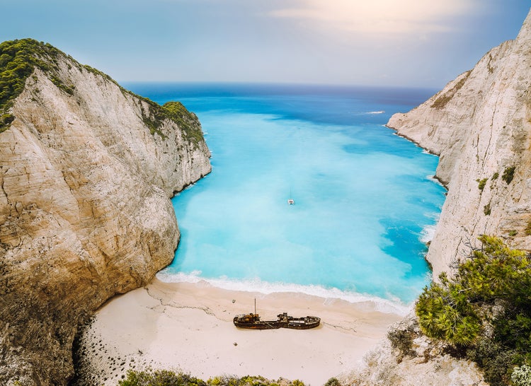 Luftaufnahme des Navagio Strandes auf Zakynthos mit hohen Kalksteinklippen, dem Meer und einem rostigen Schiffswrack auf dem Sandstrand.
