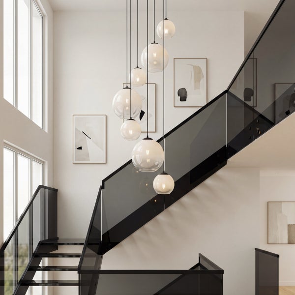 Mehrfach-Pendelleuchte mit Glaskugeln in verschiedenen Größen über einer Treppe mit Glasgeländer in einem minimalistischen, geräumigen Treppenhaus.