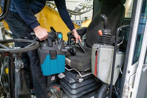 Eine Person reinigt den Innenraum einer Baumaschine mit einem tragbaren Staubsauger.
