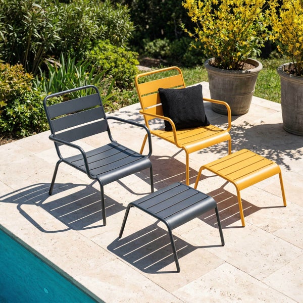 Moderne Garten-Loungesessel und Fußhocker aus Metall mit Lattendesign auf einer hellen Terrasse neben einem Pool und Pflanzen.