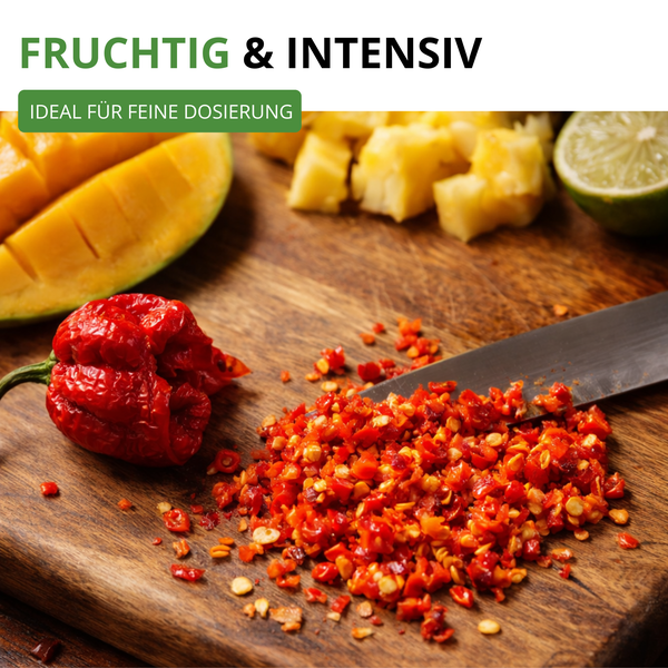 Gehackte rote Chilischoten auf einem Holzbrett mit einer ganzen Chili, Mango, Ananas und Limette.