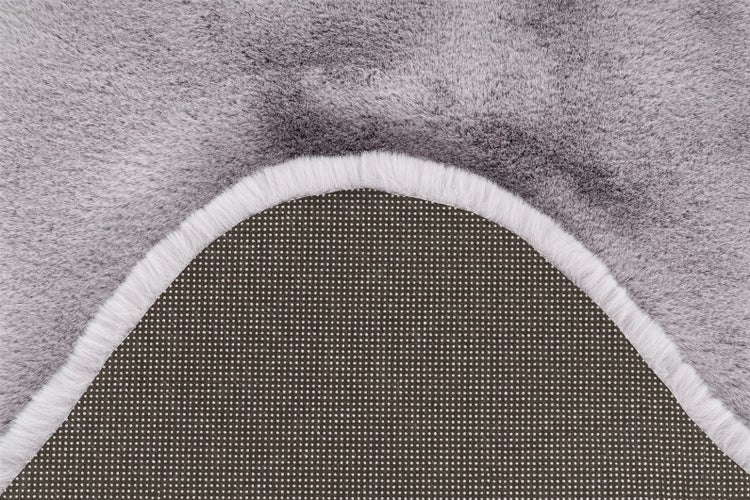 Detailansicht eines grauen Kunstfellteppichs mit weicher Oberfläche und rutschfester Rückseite mit Noppen.