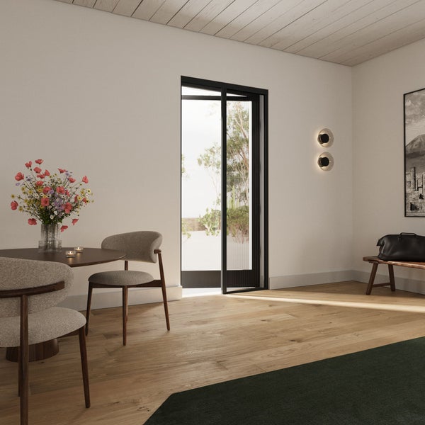 Heller, moderner Wohnraum mit rundem Holzesstisch, gepolsterten Stühlen, Parkettboden aus hellem Holz und einer schwarzen Glasschiebetür zum Garten.