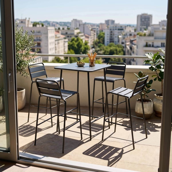 Bartisch und vier Barstühle aus Metall auf einem hellen Balkon mit Stadtblick und Topfpflanzen.