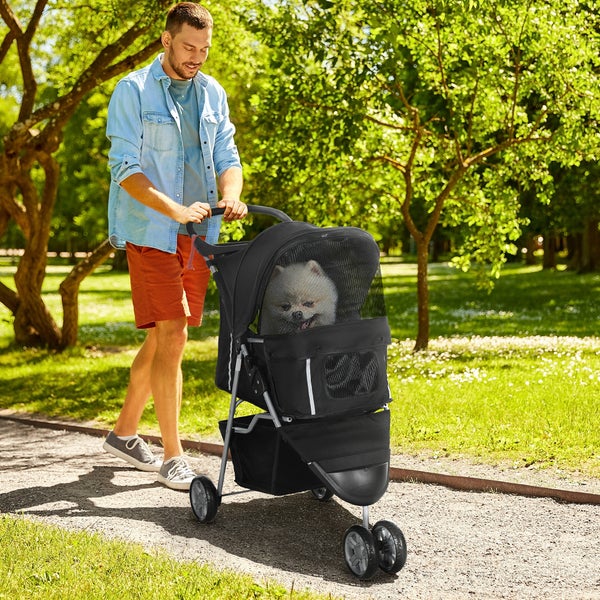 Mann schiebt einen schwarzen Tierkinderwagen mit einem kleinen Hund im Park
