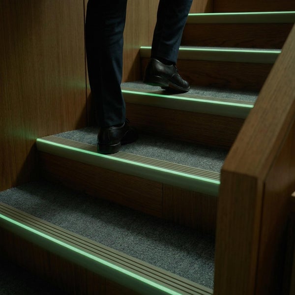 Person geht eine Treppe mit nachleuchtenden Treppenkantenprofilen in einem modern gestalteten Innenbereich hoch.