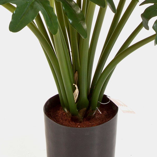 Nahaufnahme der Stiele und der Basis einer künstlichen Philodendron-Pflanze in einem schwarzen Topf mit brauner Erde.