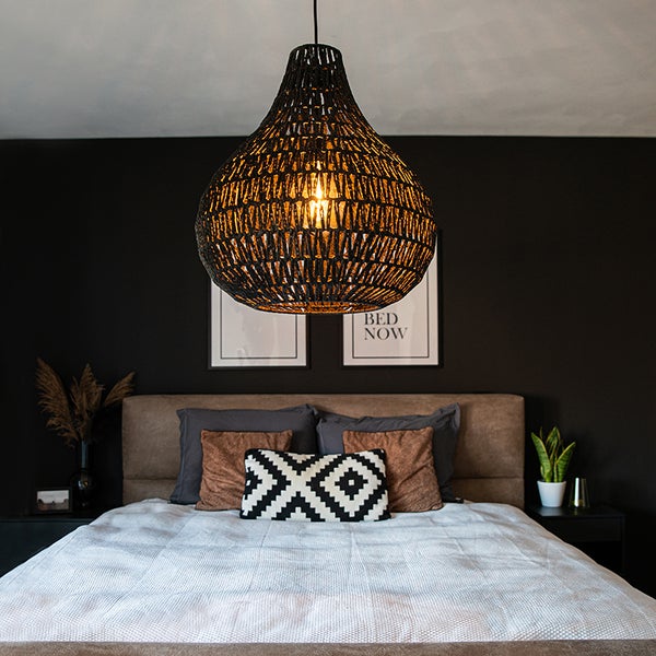 Schwarze, tropfenförmige Pendelleuchte aus Geflecht über einem Bett in einem modern eingerichteten, organisierten Schlafzimmer.