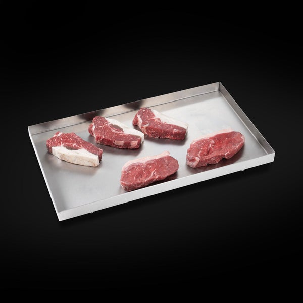 Edelstahl-Grillplatte mit fünf rohen Steaks als Grillzubehör.