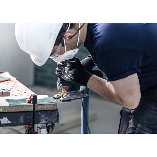 Ein Handwerker sägt mit einer Stichsäge eine Fliese. Er trägt dabei Schutzkleidung wie Helm und Schutzmaske.