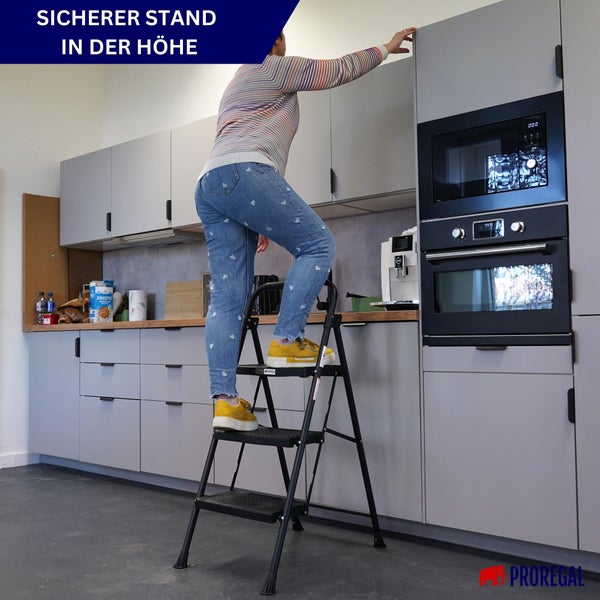Eine Person steht auf einer dreistufigen Haushaltsleiter in einer hellen, modernen Küche, um einen hohen Schrank zu erreichen. Proregal Logo.