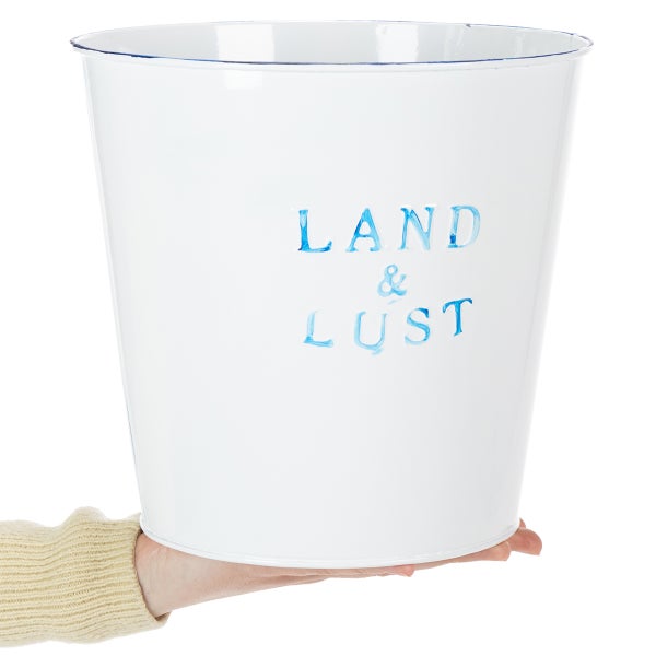 Weißer Metallblumentopf mit blauem Schriftzug Land und Lust, von einer Hand gehalten.