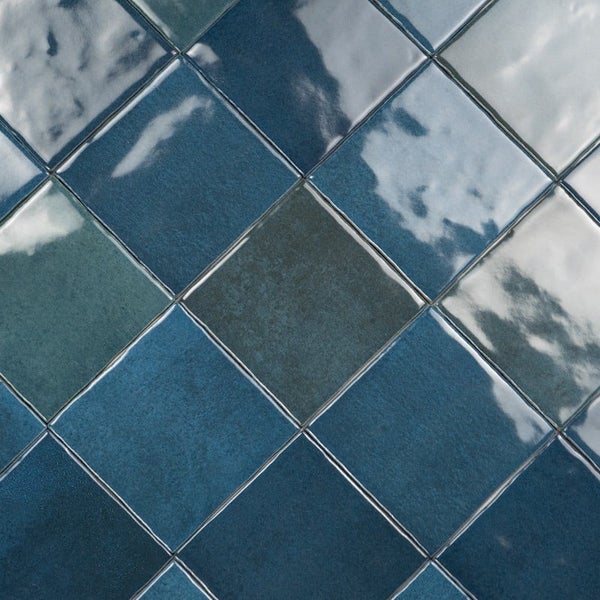 Quadratische Wandfliesen mit glänzender Oberfläche in verschiedenen Blau- und Grautönen im Verlegemuster.