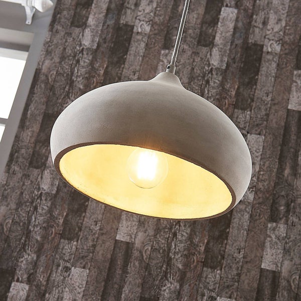 Hängeleuchte aus Beton mit goldfarbener Innenseite und leuchtendem Leuchtmittel vor einer strukturierten Wand.