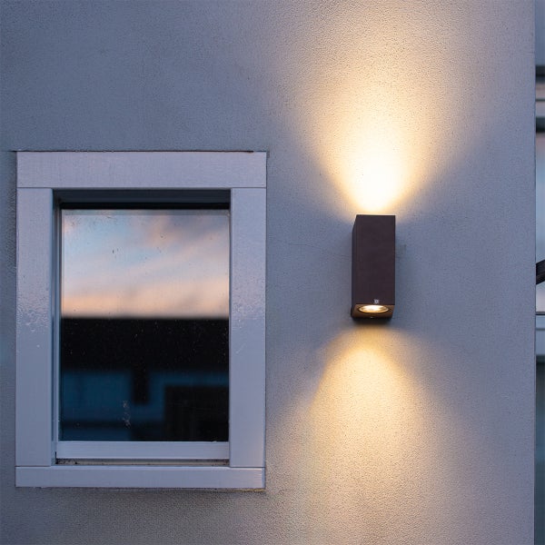 Moderne Außenwandleuchte mit Lichtaustritt nach oben und unten an einer Fassade neben einem Fenster.