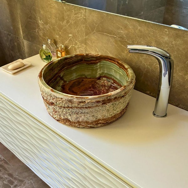 Rundes Aufsatzwaschbecken aus Naturstein auf einem weißen Badezimmerunterschrank mit Wellenmuster und moderner Chromarmatur.