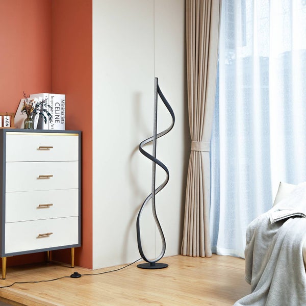 Moderne LED-Stehleuchte mit gewundenem Spiraldesign in einem hellen Wohnzimmer neben einer weißen Kommode und hellen Vorhängen.