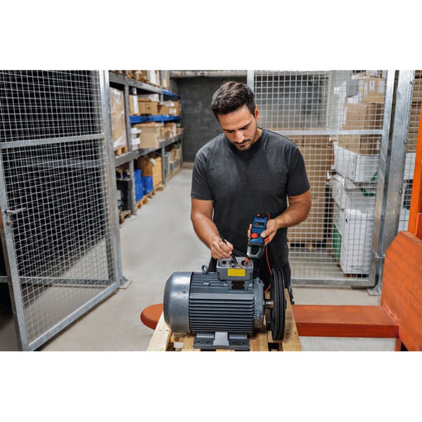 Ein Mann misst eine Elektromaschine mit einem Strommessgerät in einem Lager.