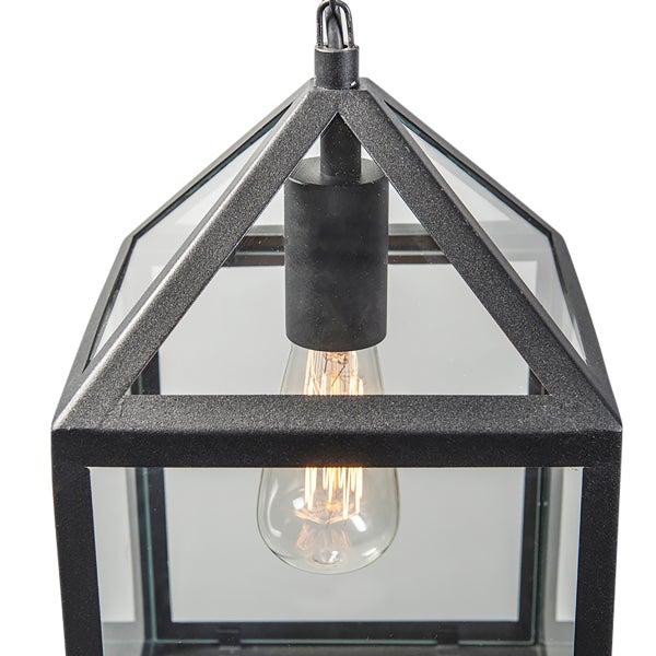 Pendelleuchte in Laternenform aus schwarzem Metall und Glas mit sichtbarem Filament-Leuchtmittel.