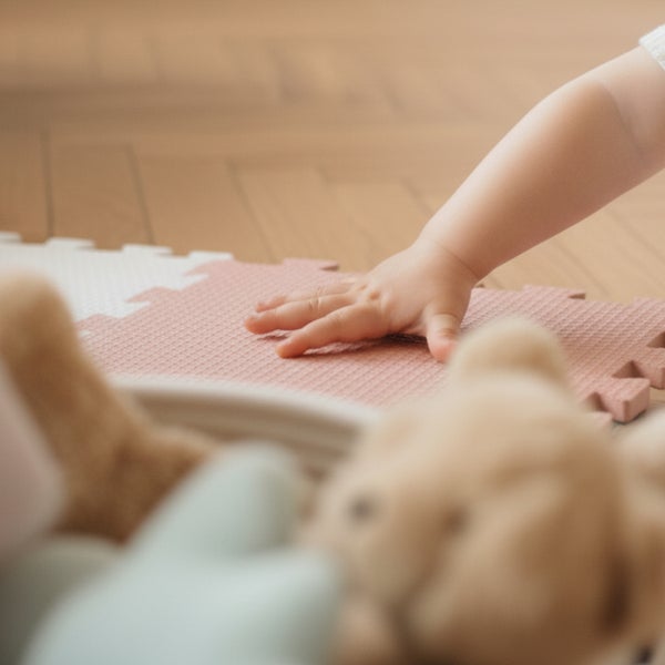 Ein Kinderhändchen liegt auf einer strukturierten Puzzlematte für Kinder, die auf einem Boden mit Fischgrätmuster liegt.