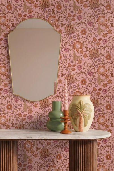 Vliestapete mit floralem Muster, Wandspiegel mit Goldrahmen, Marmortisch mit Vasen und Kerzenhalter in einem hellen Zimmer.