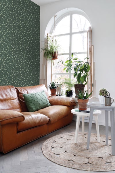 Wohnzimmer mit braunem Ledersofa, grüner Kissen und runden Beistelltischen