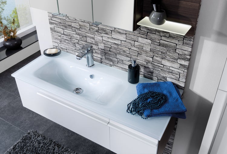 Moderner weißer Waschtisch mit rechteckigem Waschbecken, verchromter Armatur und einer Rückwand in Steinoptik.